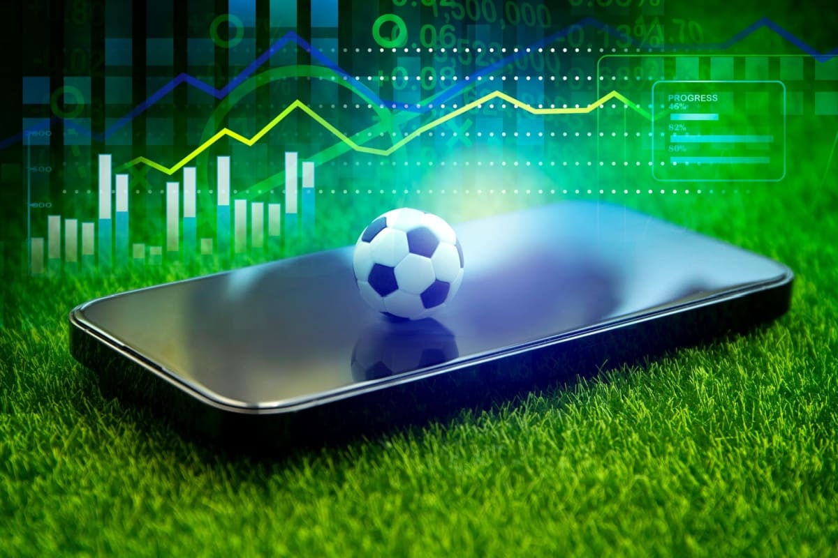 telefon mobil si minge de fotbal pe gazonul unui teren de fotbal cu statistici in fundal