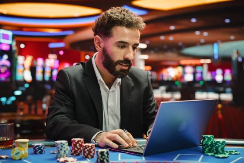barbat jucand poker in fata unui laptop cu jetoane in jur