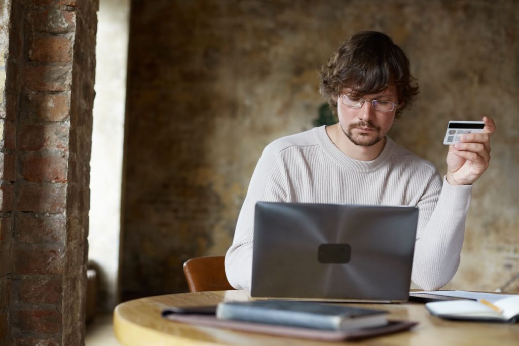 barbat introducand date pe un laptop, tinand in mana un card bancar
