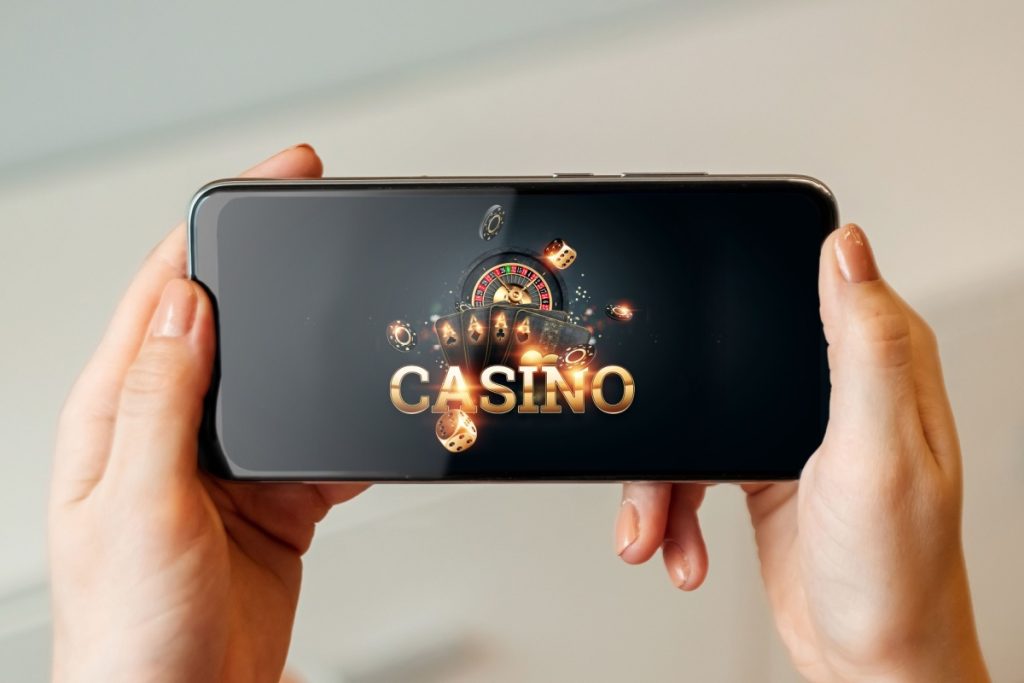 doua maini tinand un telefon mobil pe care ruleaza o aplicatie de cazino online