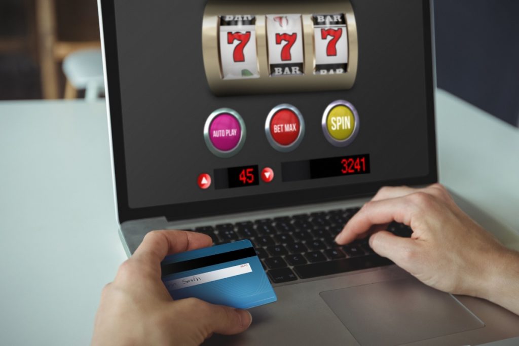 persoana in fata unui laptop, jucand un slot simplu online, cu cardul de credit in mana