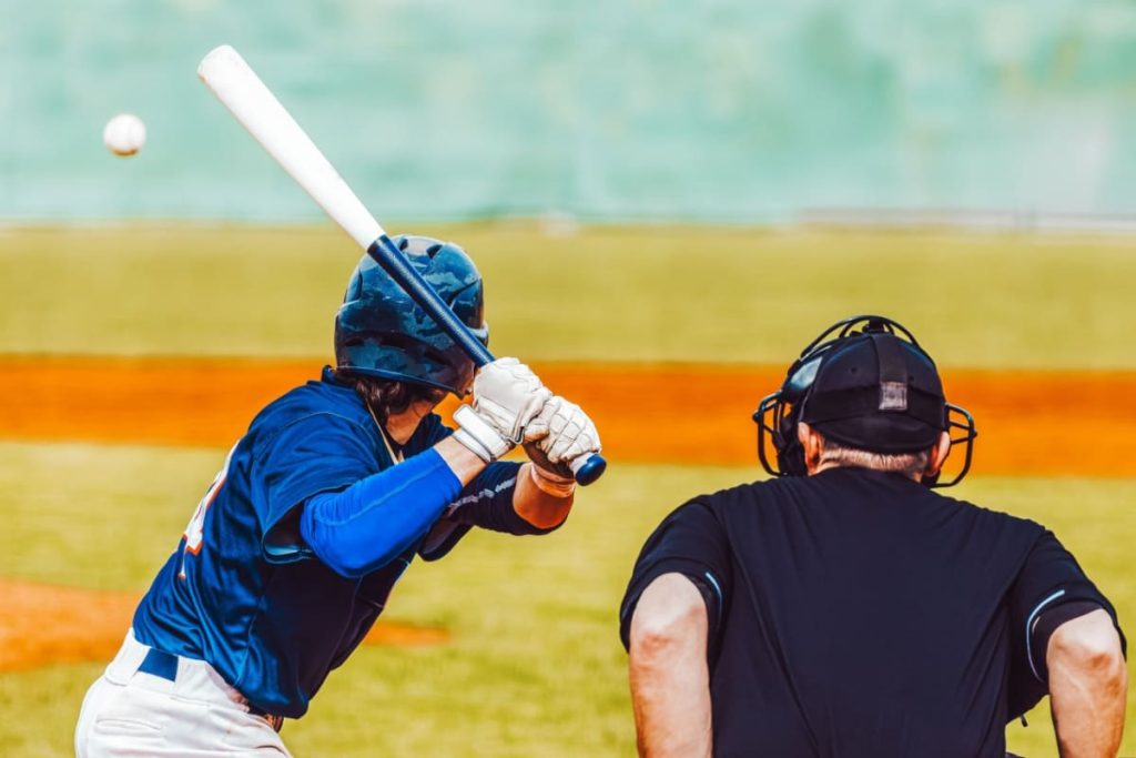 jucator de baseball pregatit sa loveasca mingea, cu un arbitru alaturi