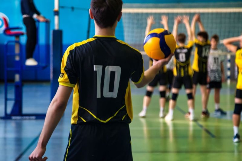 jucator de volei pregatindu-se de inceperea meciului, cu ceilalti jucatori la mijlocul terenului