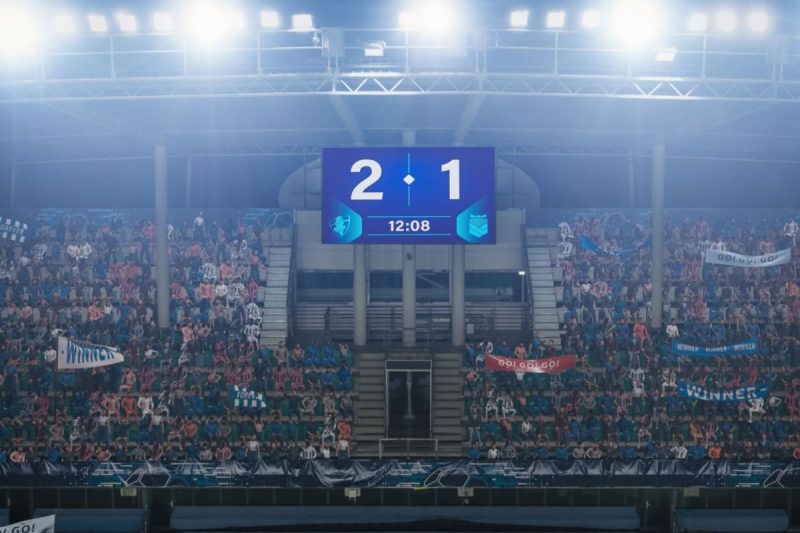 tribuna in timpul unui meci de fotbal cu suporteri si tabela de scor