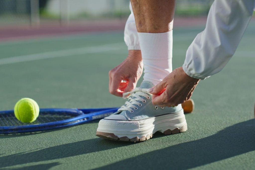 jucator de tenis pe teren, legandu-se la siret, cu o minge si racheta alaturi