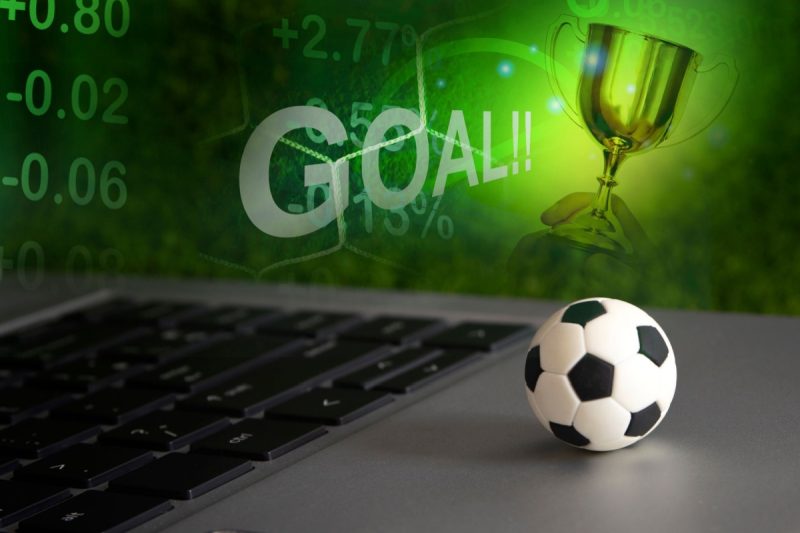 o minge mica de fotbal pe un laptop, cu statistici, cote si o cupa in fundal