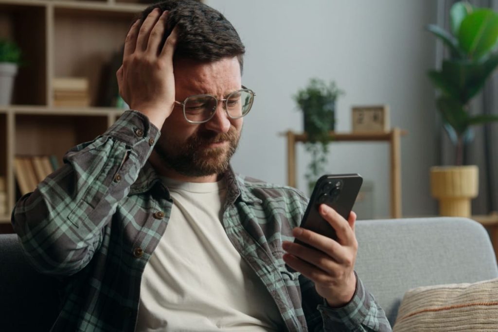barbat trist, cu o mana la cap, tinand in cealalta mana un telefon mobil