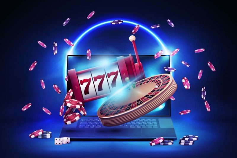 laptop cu o ruleta, un slot mecanic, zaruri si jetoane de cazino in jur
