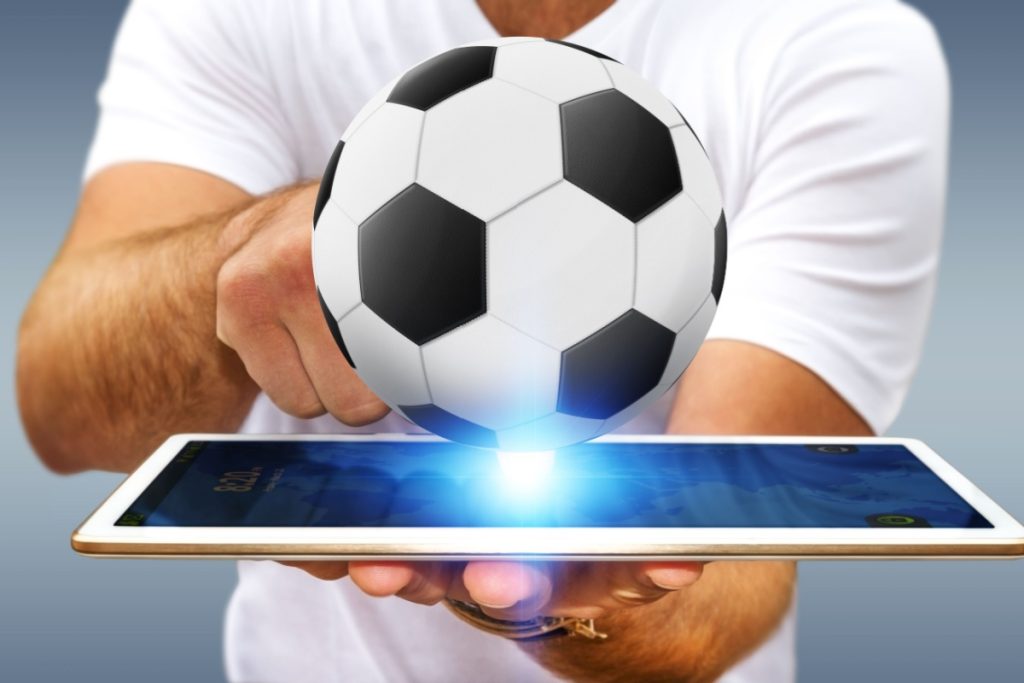 barbat tinand in mana o tableta pe care sta sprijinita o minge de fotbal
