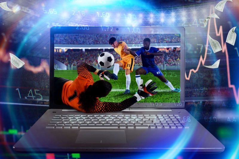 laptop afisand un meci de fotbal in desfasurare, cu grafice, cote si bancnote in jur