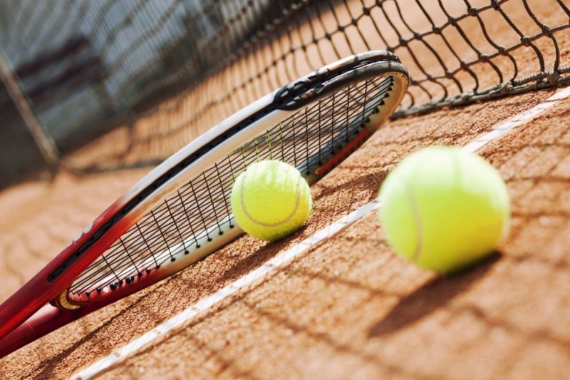 racheta si doua mingi de tenis pe un teren cu zgura