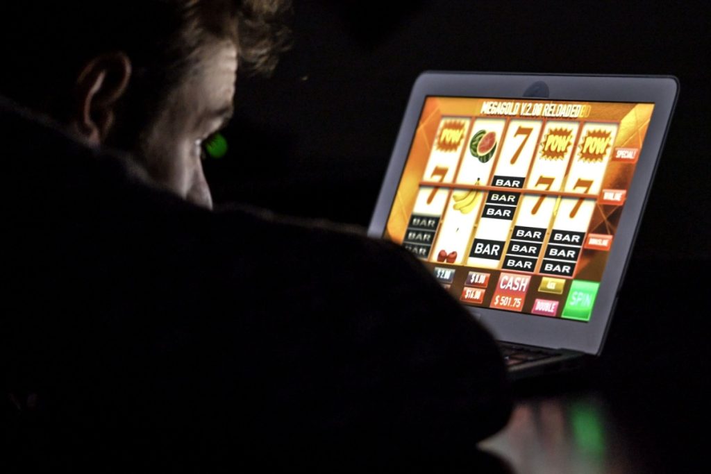 barbat abatut intr-o camera intunecata, jucand un slot online pe laptop