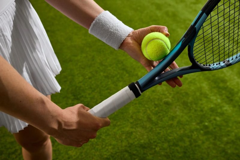 jucatoare de tenis pe un teren cu iarba, tinand in mana o minge si o racheta