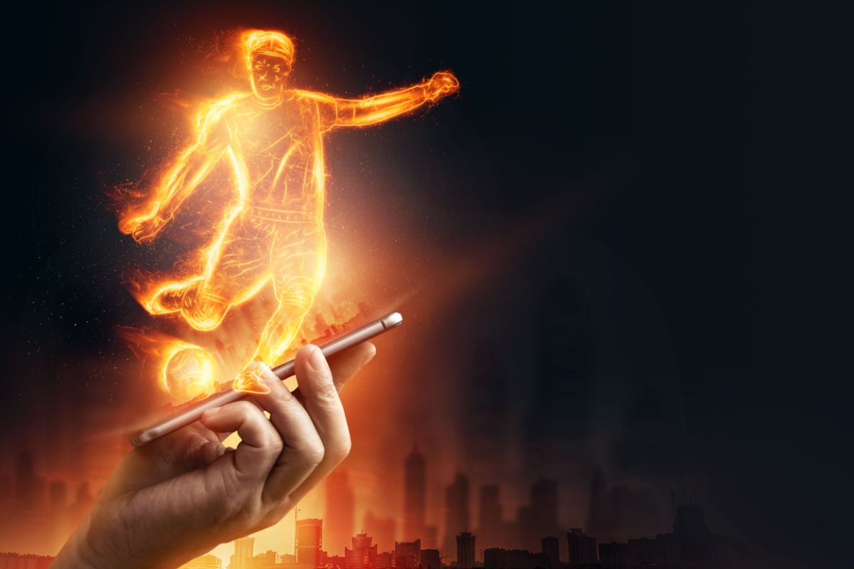 mana tinand un telefon mobil din care se proiecteaza o holograma a unui jucator de fotbal