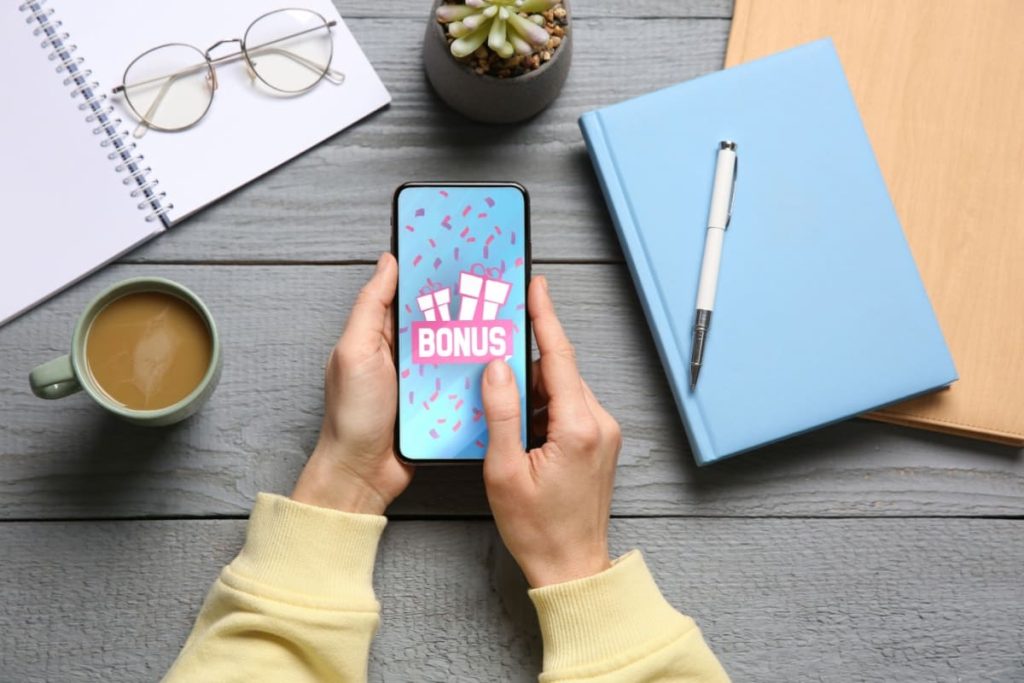persoana asezata la masa, cu un telefon in mana, pe care este afisata o notificare de bonus