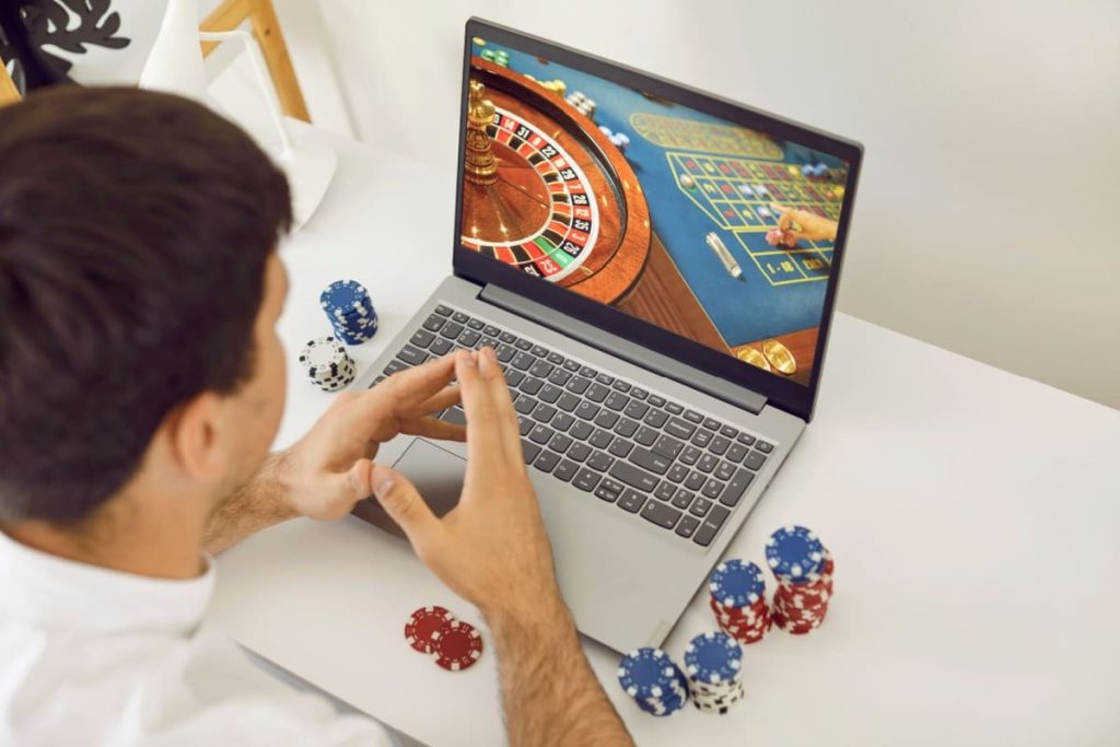 barbat cu jetoane alaturi, in fata unui laptop pe care ruleaza un joc de cazino live online