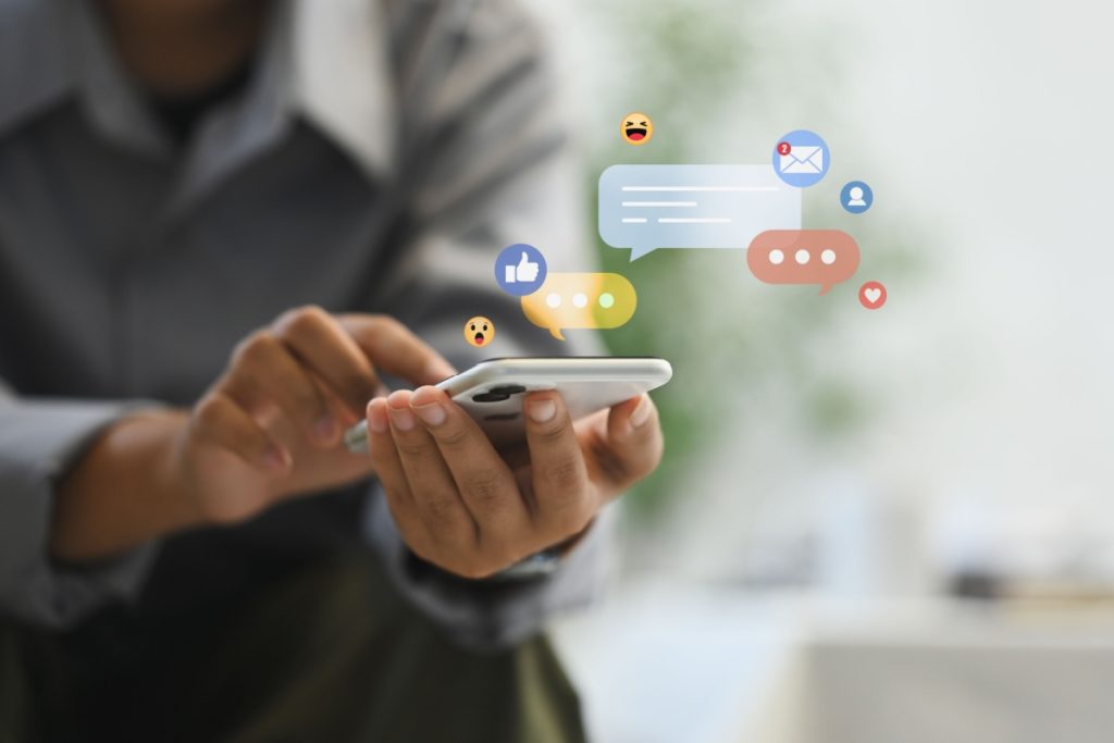 barbat tinand in mana un telefon mobil, cu notificari de mesaje si reactii in jur