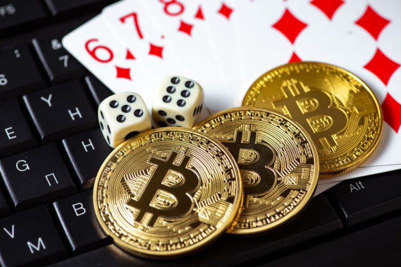 jetoane cu sigla unei criptomonede, zaruri si carti de joc pe o tastatura de laptop