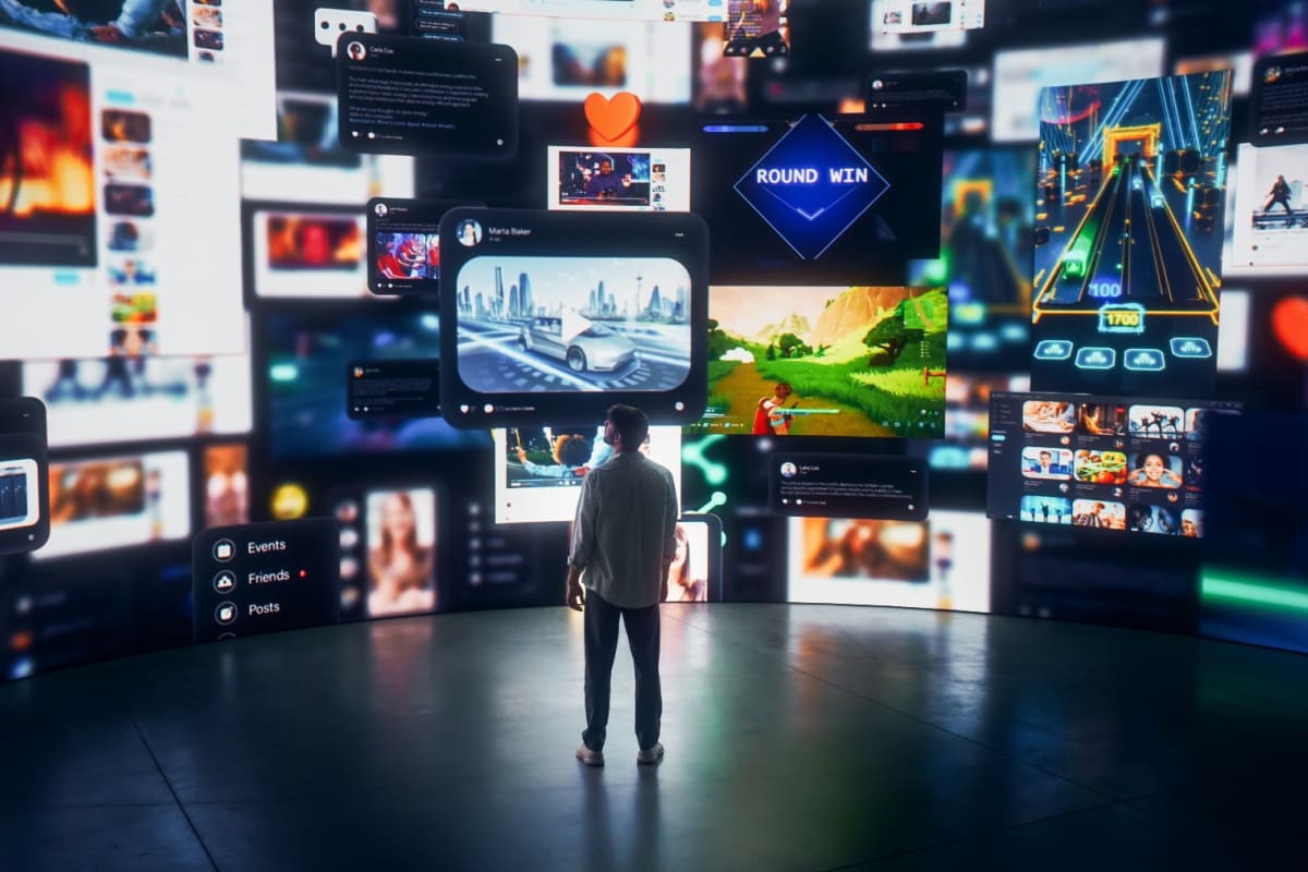 barbat stand in picioare in fata mai multor ecrane pe care sunt afisate diverse pagini web, jocuri si mesaje