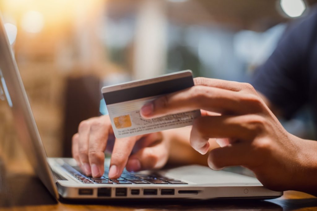 persoana in fata unui laptop, cu un card de credit in mana