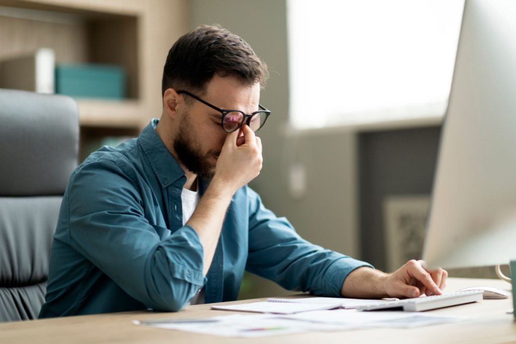 barbat obosit asezat la birou, frecandu-se la ochi