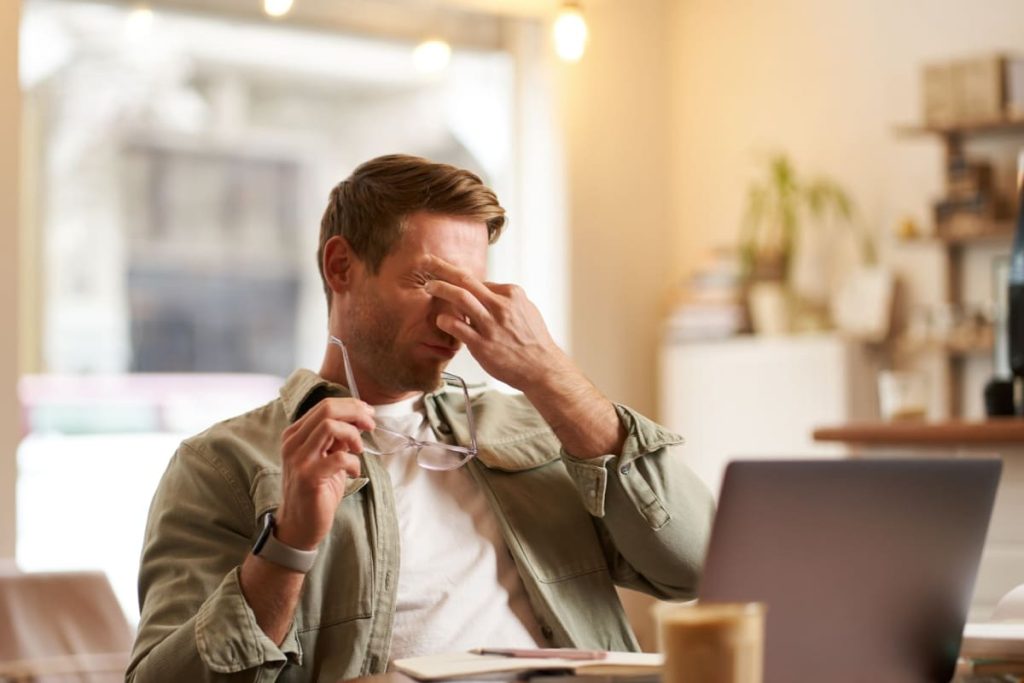 barbat obosit, cu mainile la ochi, in fata unui laptop